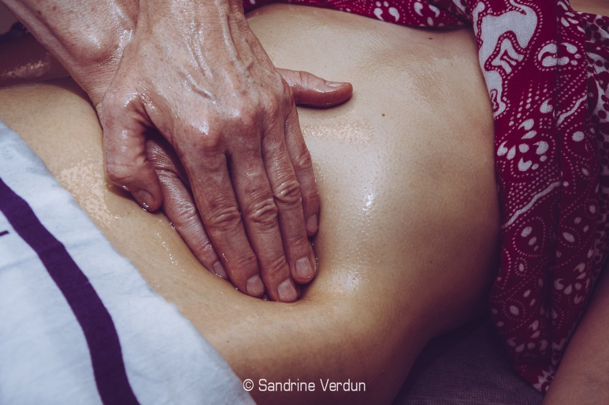 Mains d'une praticienne massant doucement un ventre avec de l'huile de soin pour un massage relaxant